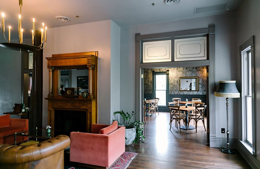 Elegant living room with chandelier, vintage fireplace, and view into a stylish dining area with wooden chairs.