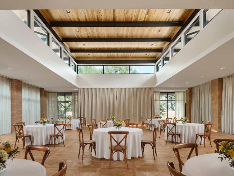 Elegant banquet hall with round tables white tablecloths and wooden chairs under a wooden ceiling