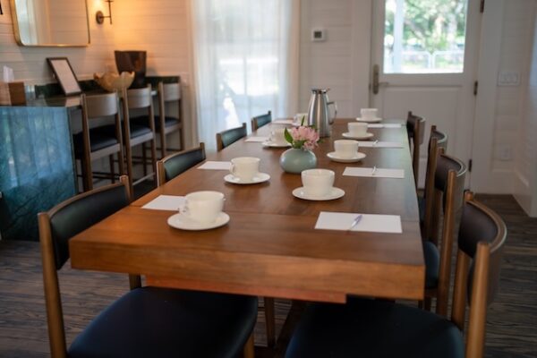 Cozy meeting room with a wooden table set for eight with teacups, notebooks, and a flower vase centerpiece