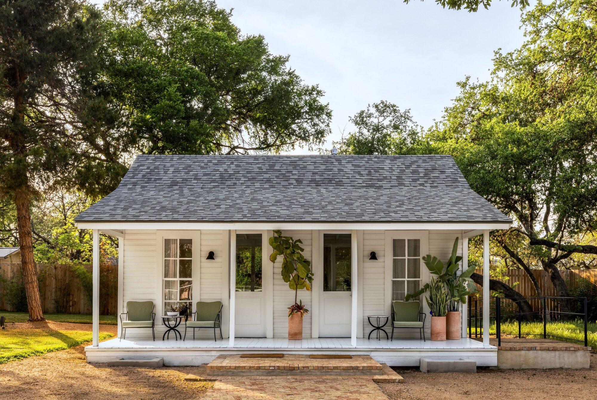 Charming white cottage with porch surrounded by trees and a sunny yard.