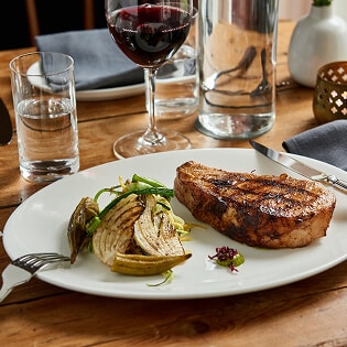 Grilled steak with roasted vegetables on a white plate served with red wine on a wooden table