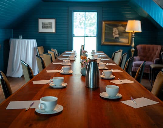 Meeting room with a long wooden table set for coffee and notepads in a cozy blue-paneled space