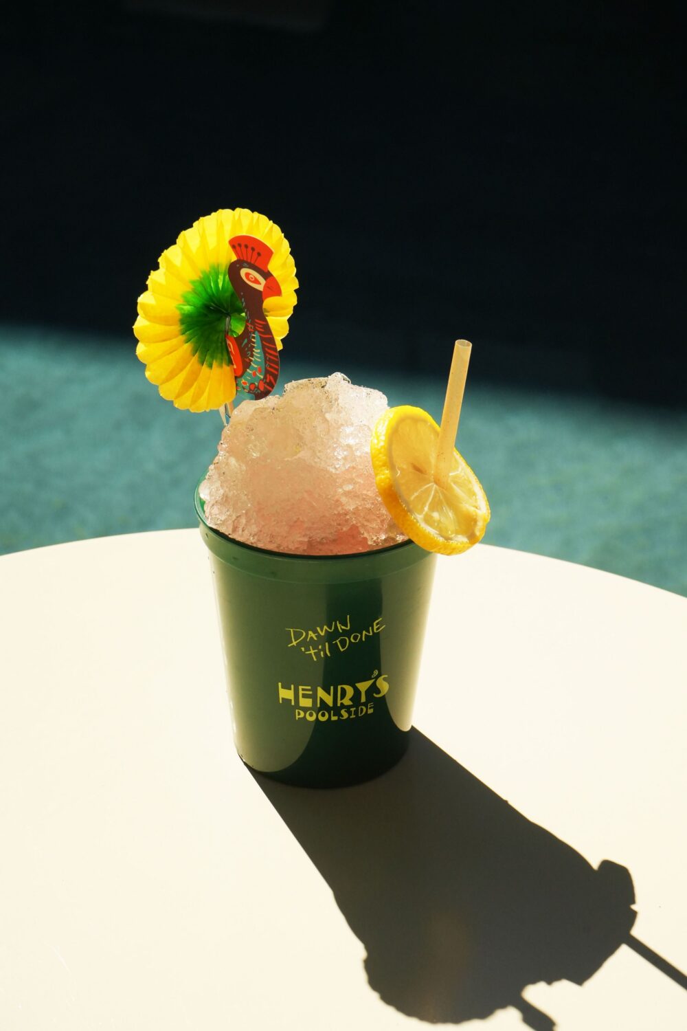 Colorful cocktail with crushed ice lemon slice and straw in a green cup with a paper bird decoration