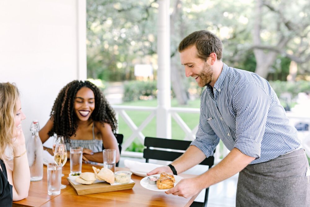 Waiter serves food to smiling women at outdoor restaurant table