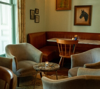 Cozy cafe corner with a round table and plush chairs beside a leather banquette and horse artwork.
