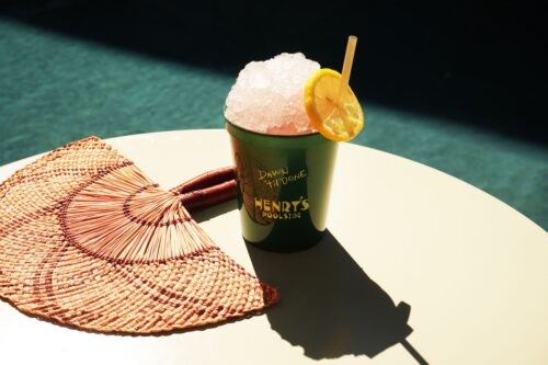 Icy drink with lemon slice and straw by the pool on a sunny day next to a woven fan.