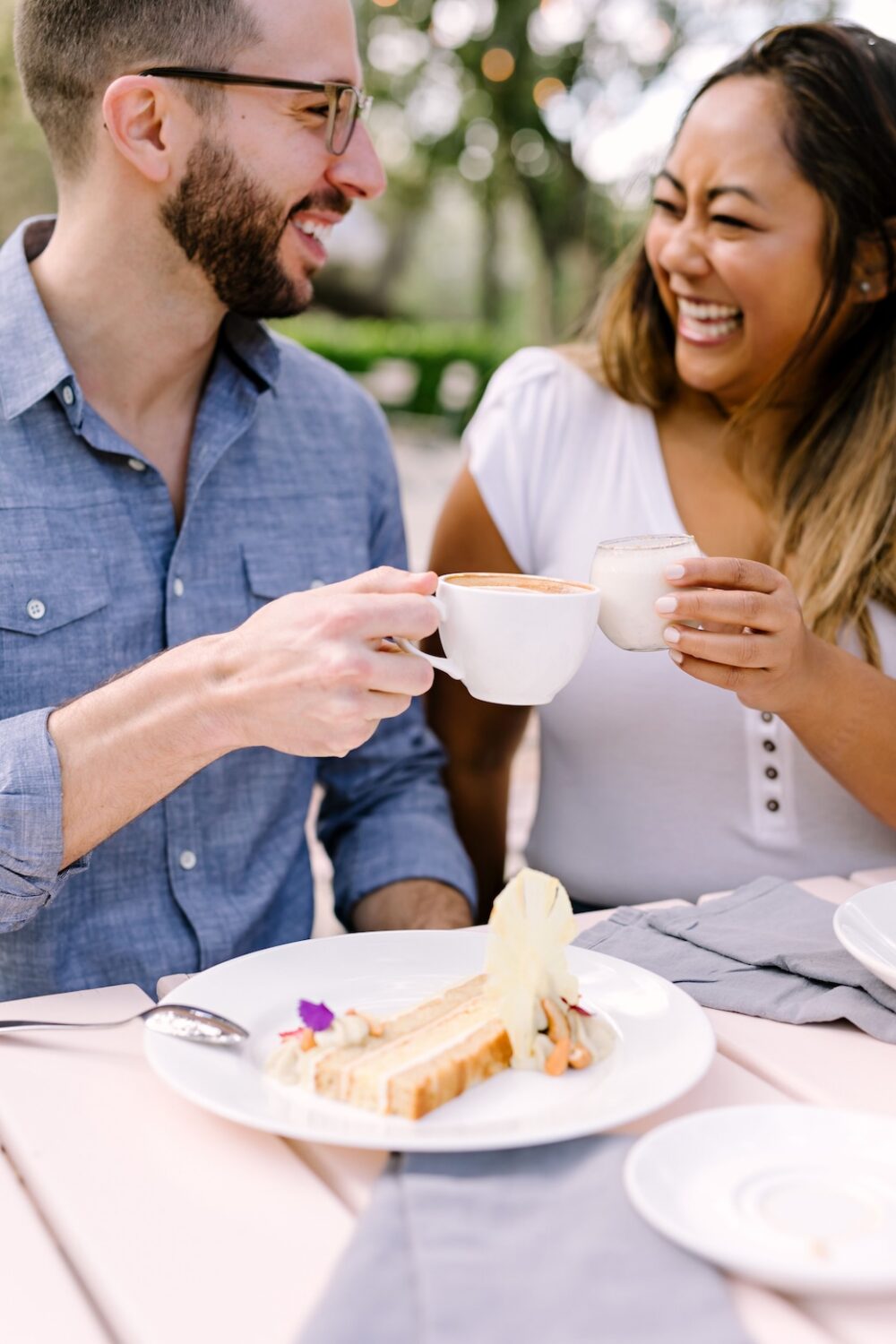 Couple enjoying coffee and dessert outdoors while laughing together