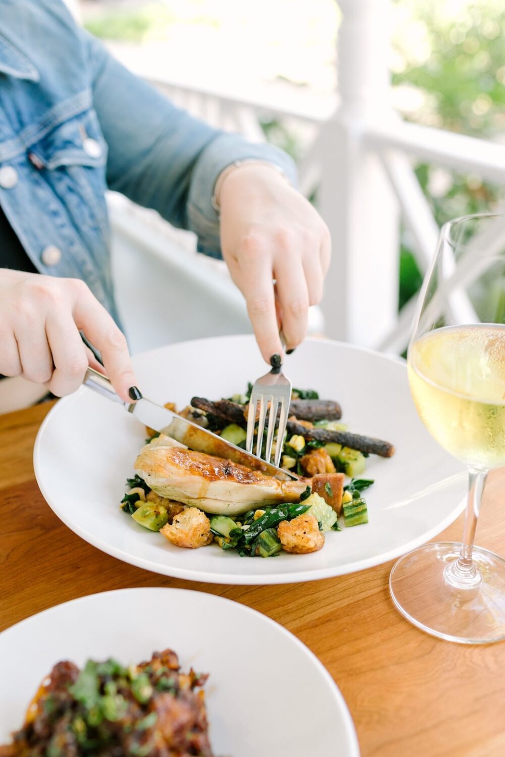 Person enjoying a grilled chicken salad with a glass of white wine on a sunny patio