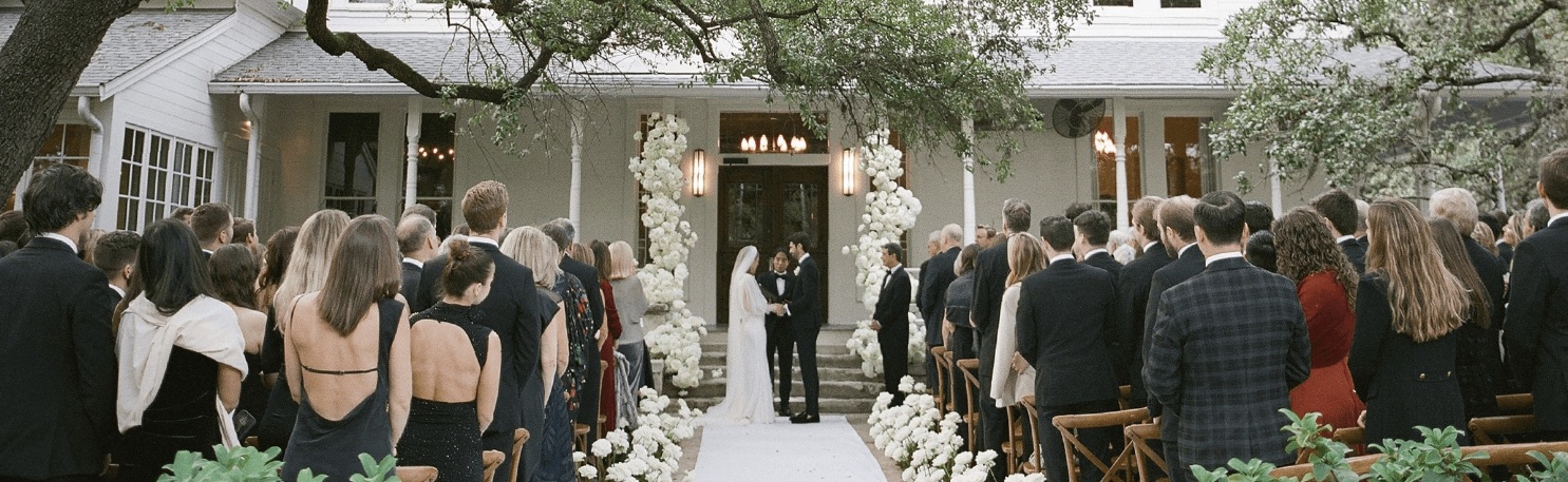 Outdoor wedding ceremony with bride and groom at elegant venue surrounded by guests and white floral decorations