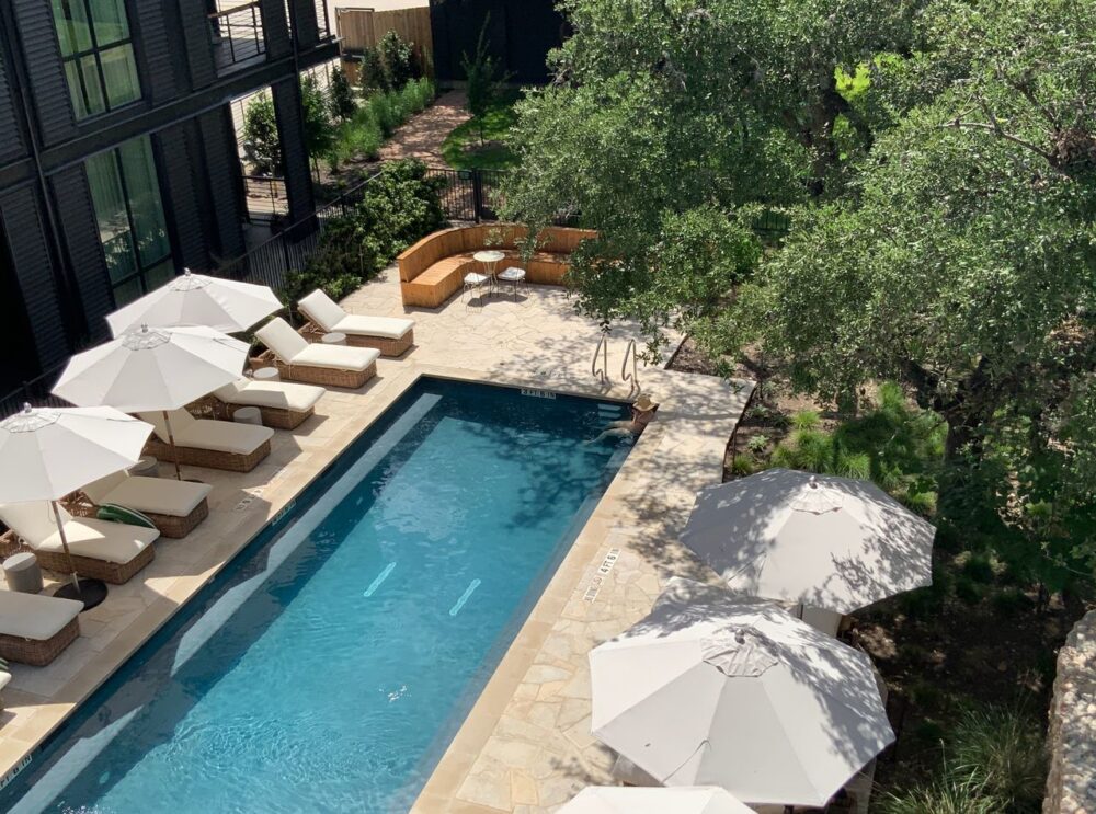 Outdoor pool area with loungers and umbrellas surrounded by trees and greenery